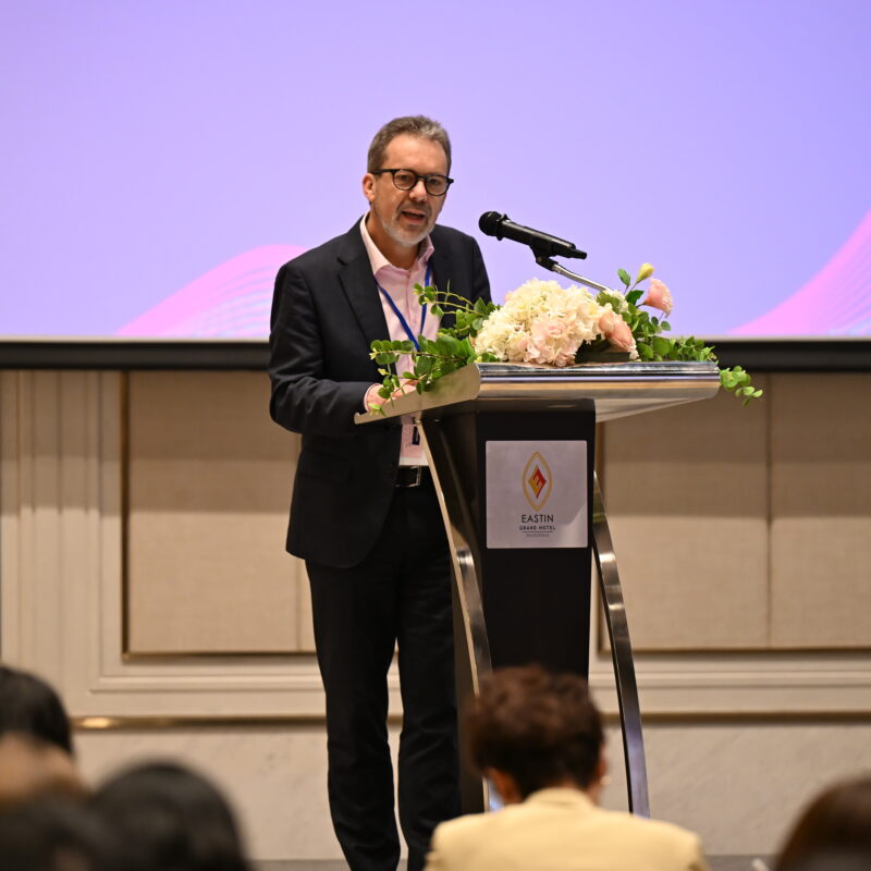 Matthias Ruth speaking at a podium at event with Valuing Voices screen in background.