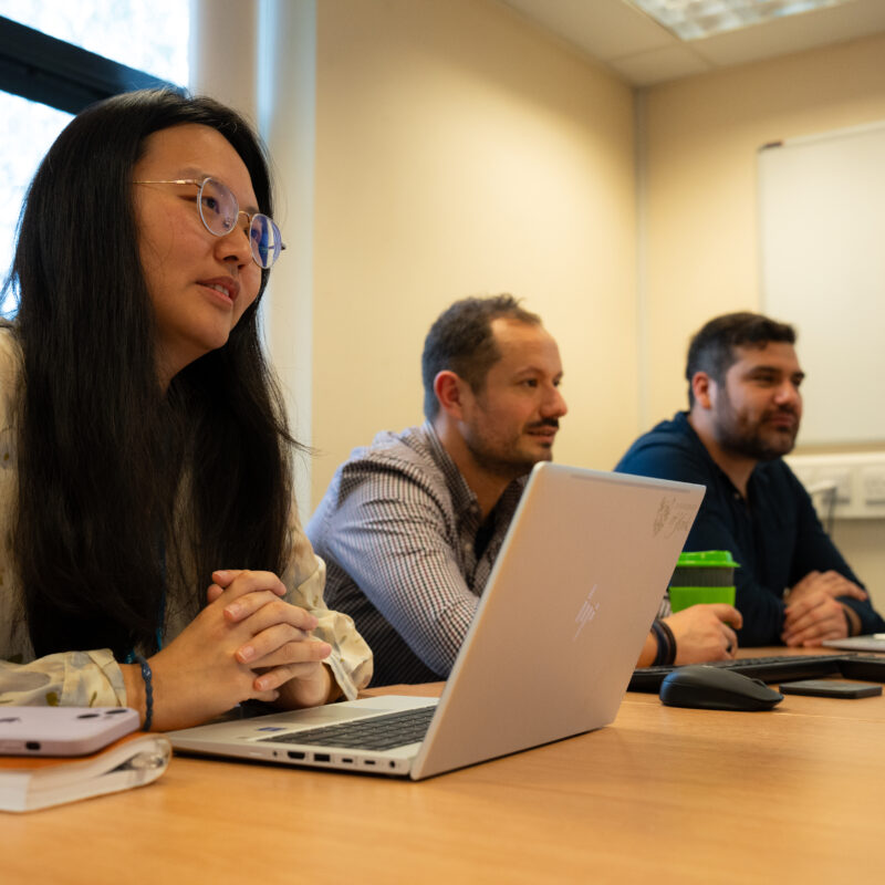 Three researchers sit at a table with laptops in front of them.