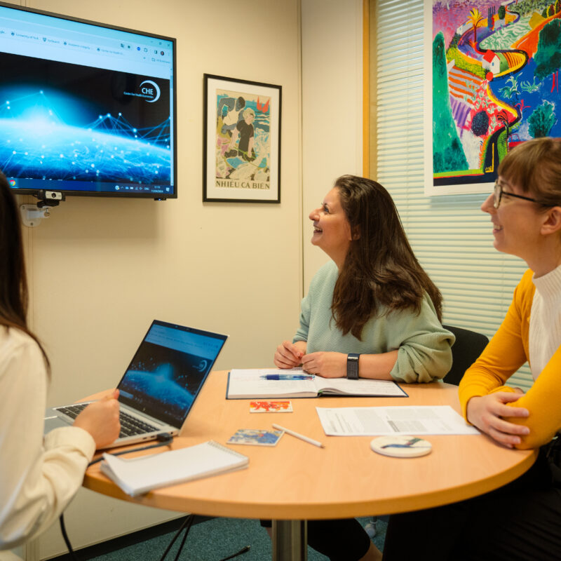 Three researchers sit at a desk, looking at an image on a monitor screen.